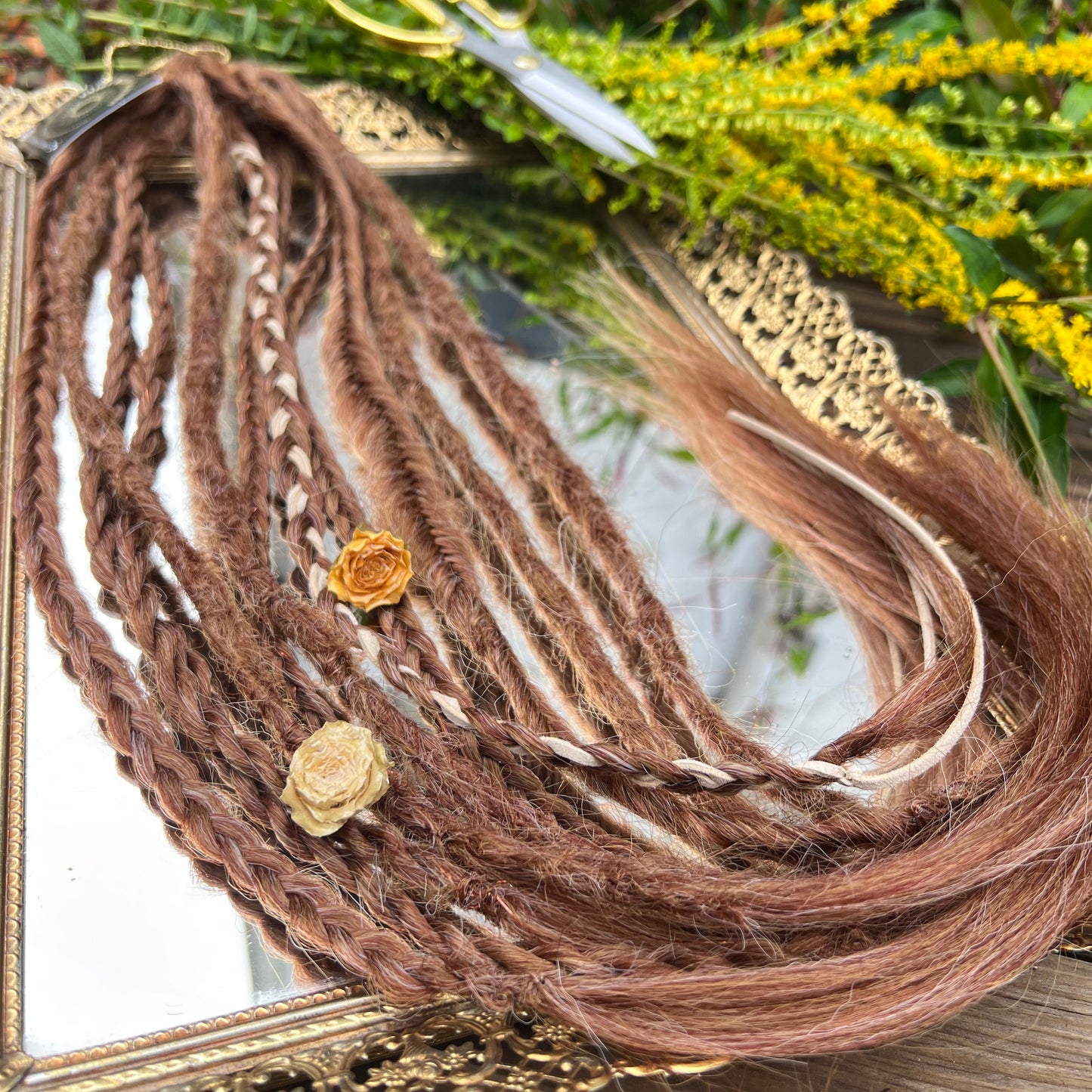 Brown braided hair extensions on a decorative mirror with greenery in the background