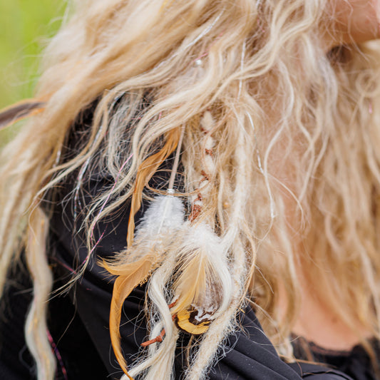 Close-up of a person with long, wavy blond hair featuring feathers and beads.