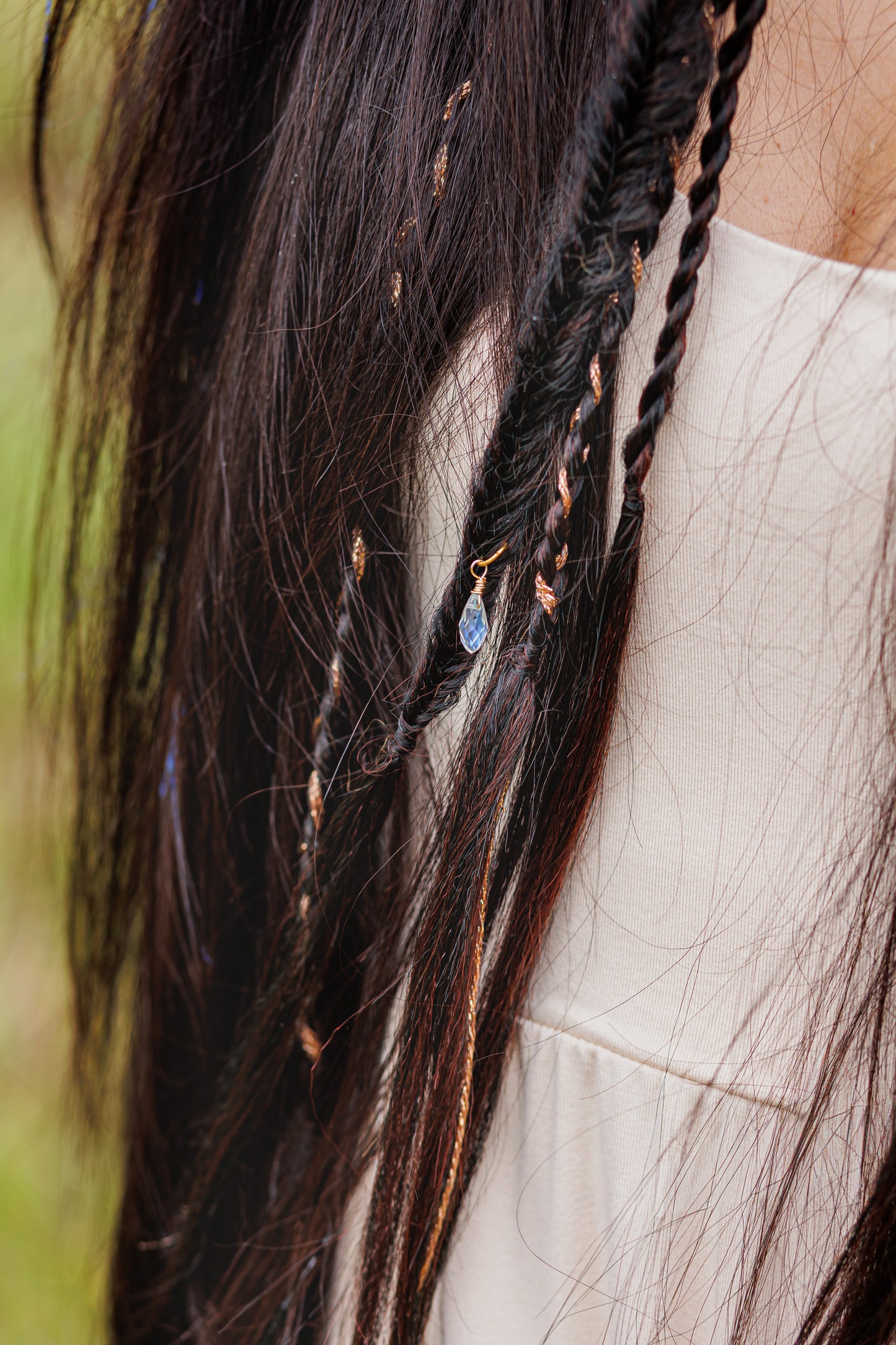 Long dark hair with small braids, beaded accents, and blue charm, styled in boho fashion.