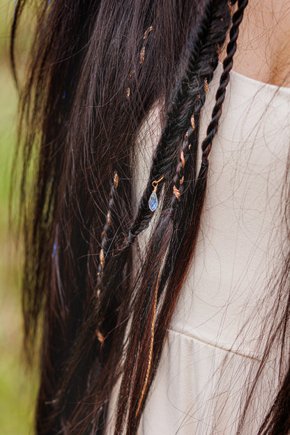 Long dark hair with small braids, beaded accents, and blue charm, styled in boho fashion.