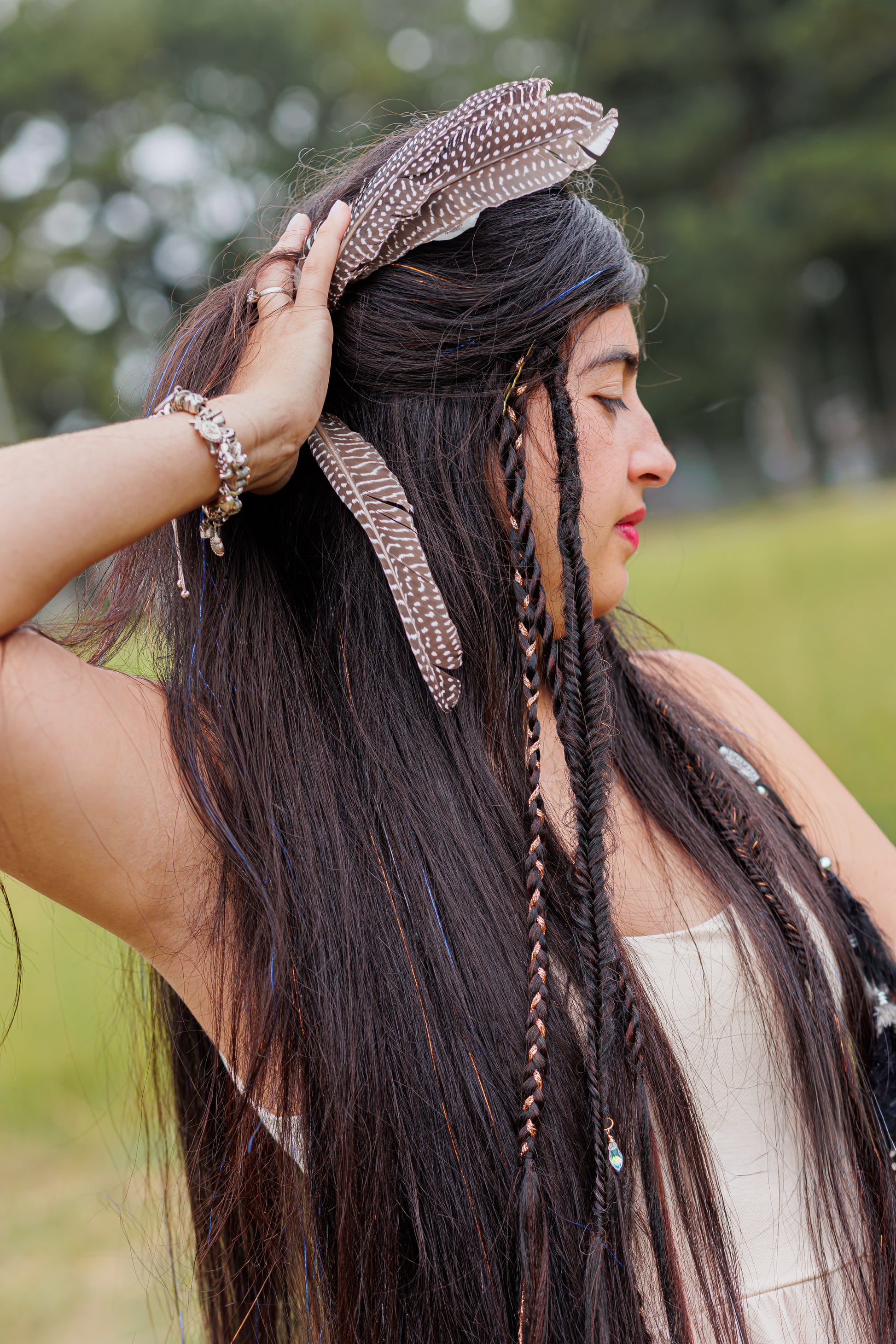 Long dark textured hair with braids, beads, and feathers, styled in boho fashion outdoors.