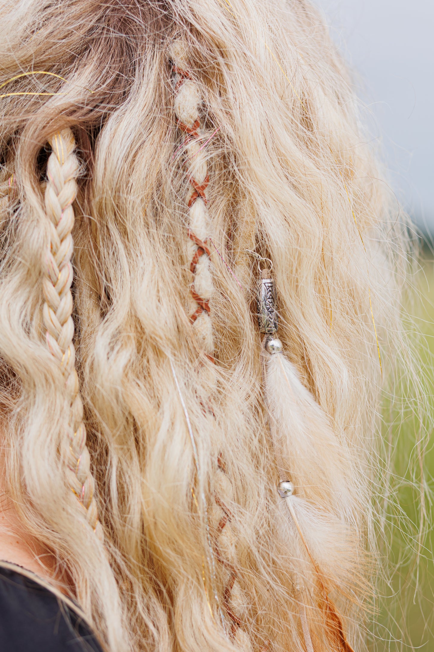 Close-up of blonde hair with braids and decorative elements against a blurred natural background
