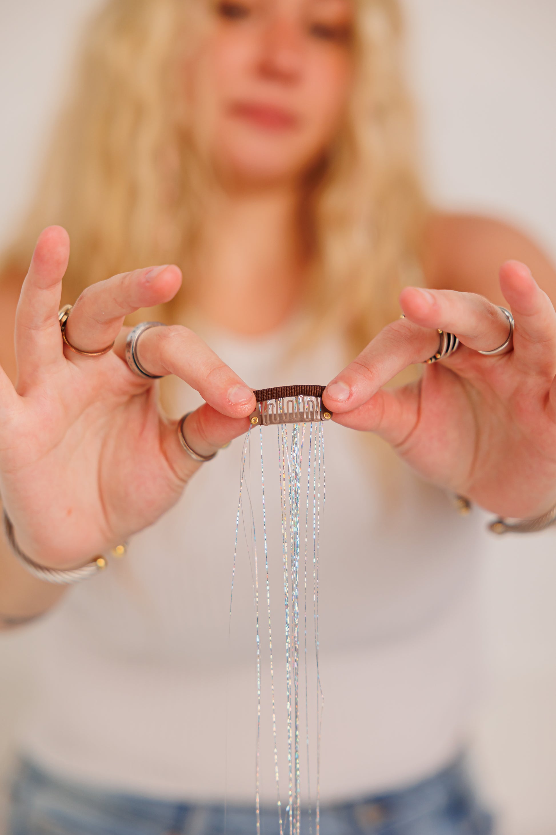 Person holding a hair accessory with silver strands and with dangling beads, blurred background