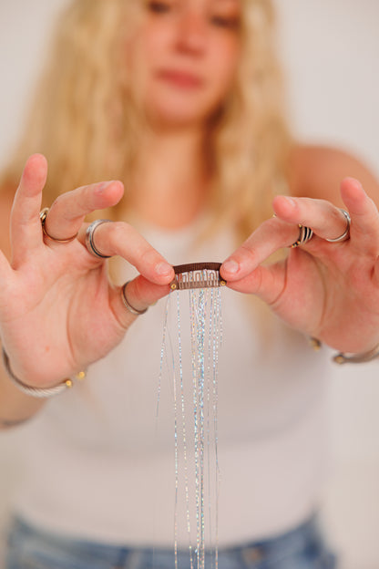 Person holding a hair accessory with silver strands and with dangling beads, blurred background