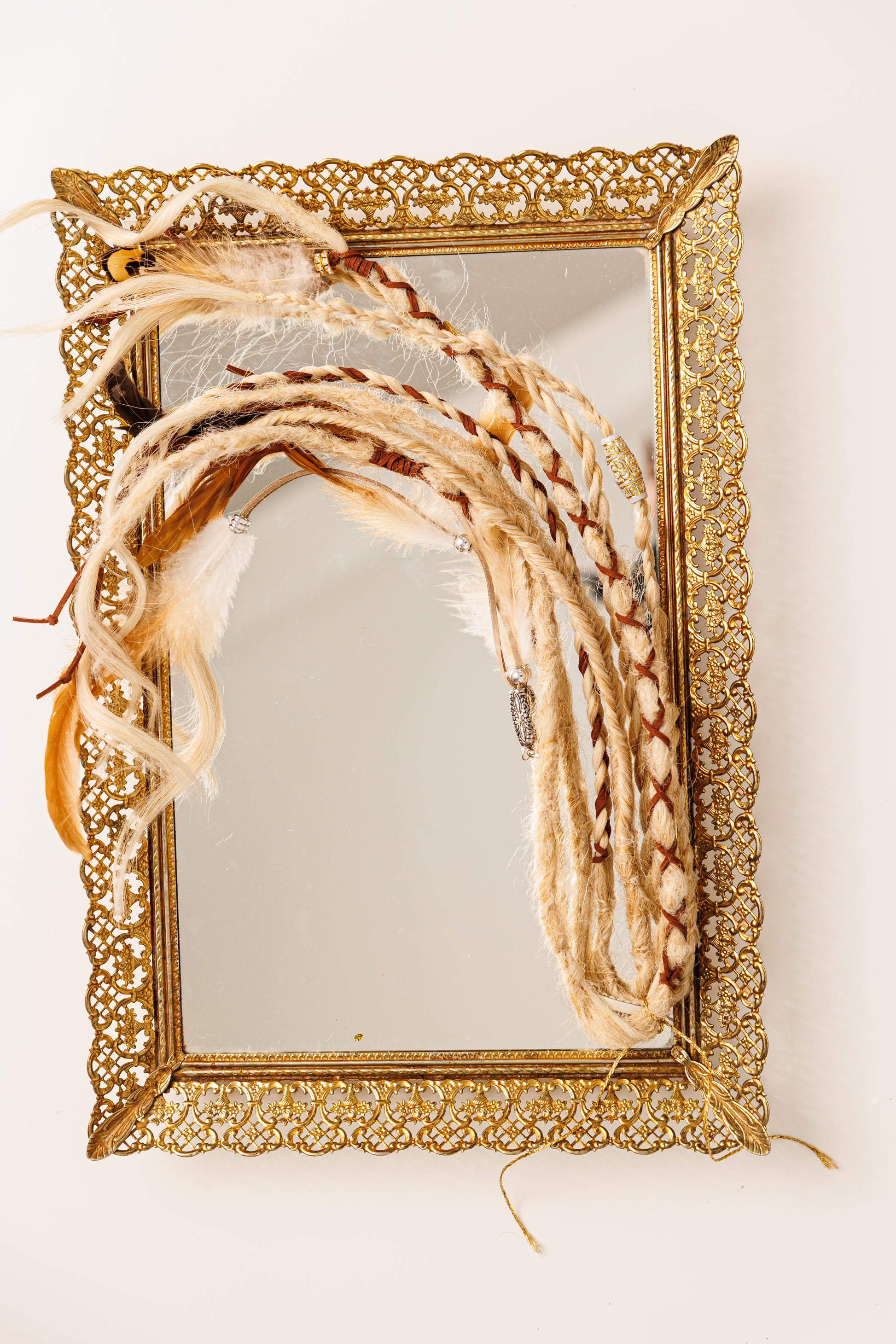 Decorative gold-framed mirror with braided decorative elements on a white background