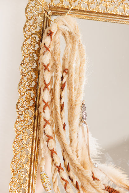 light blond Braided hair design and tassels hanging on a gold-framed mirror.