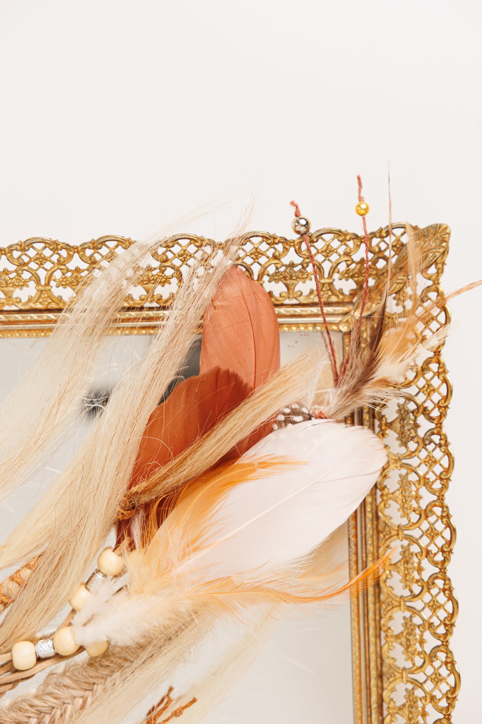Decorative arrangement of feathers and beads on a gold ornate frame.