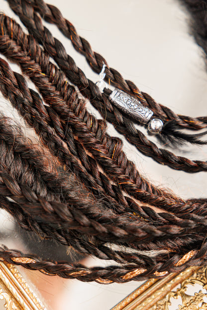 Dark brown twisted hair strands with engraved metallic charm on ornate gold mirror surface.