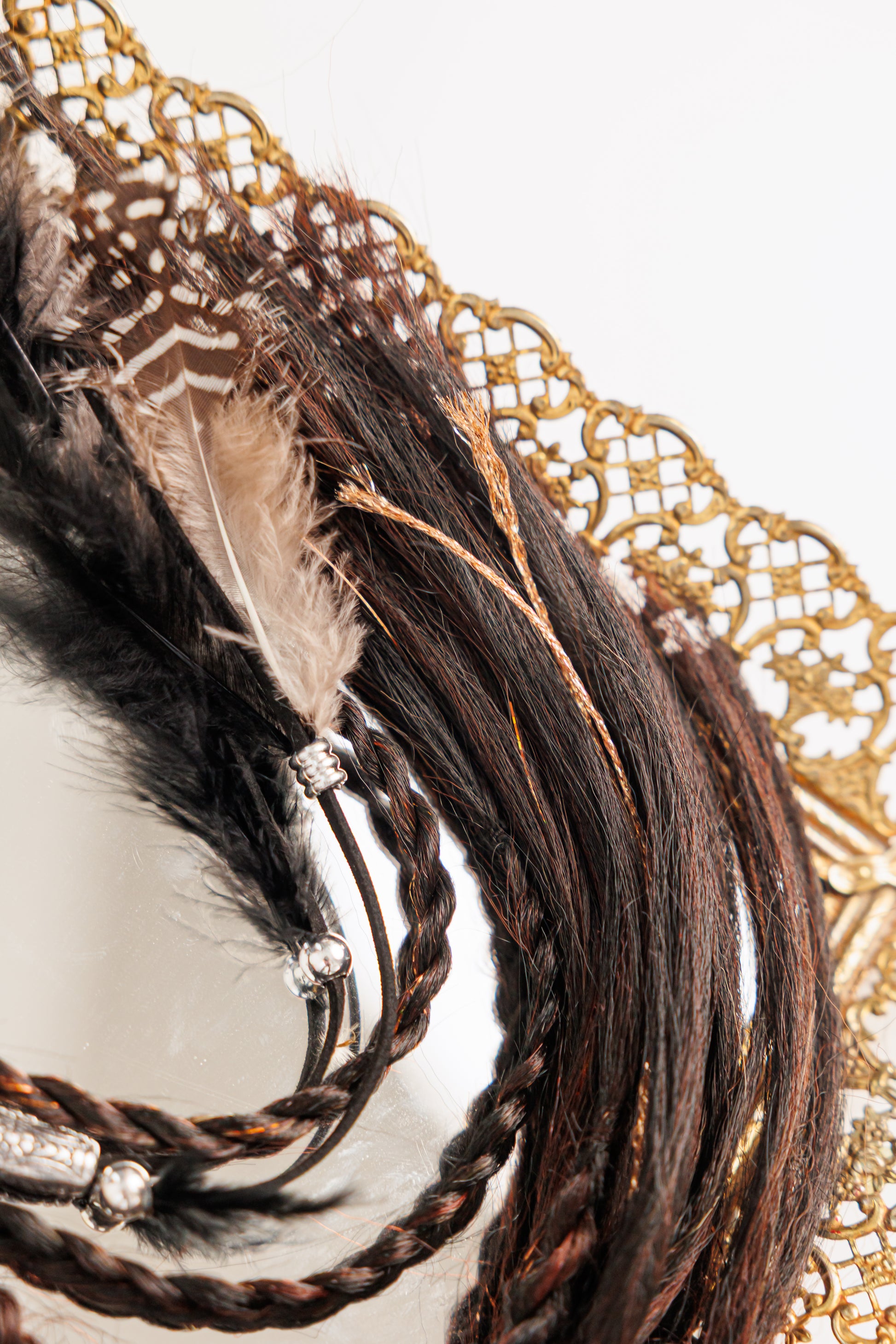 Close-up of a decorative hairpiece with braided hair, feathers, and beads on a white background.