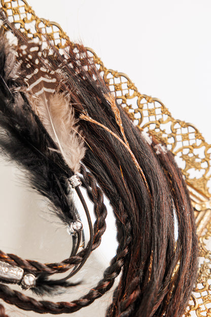 Close-up of a decorative hairpiece with braided hair, feathers, and beads on a white background.