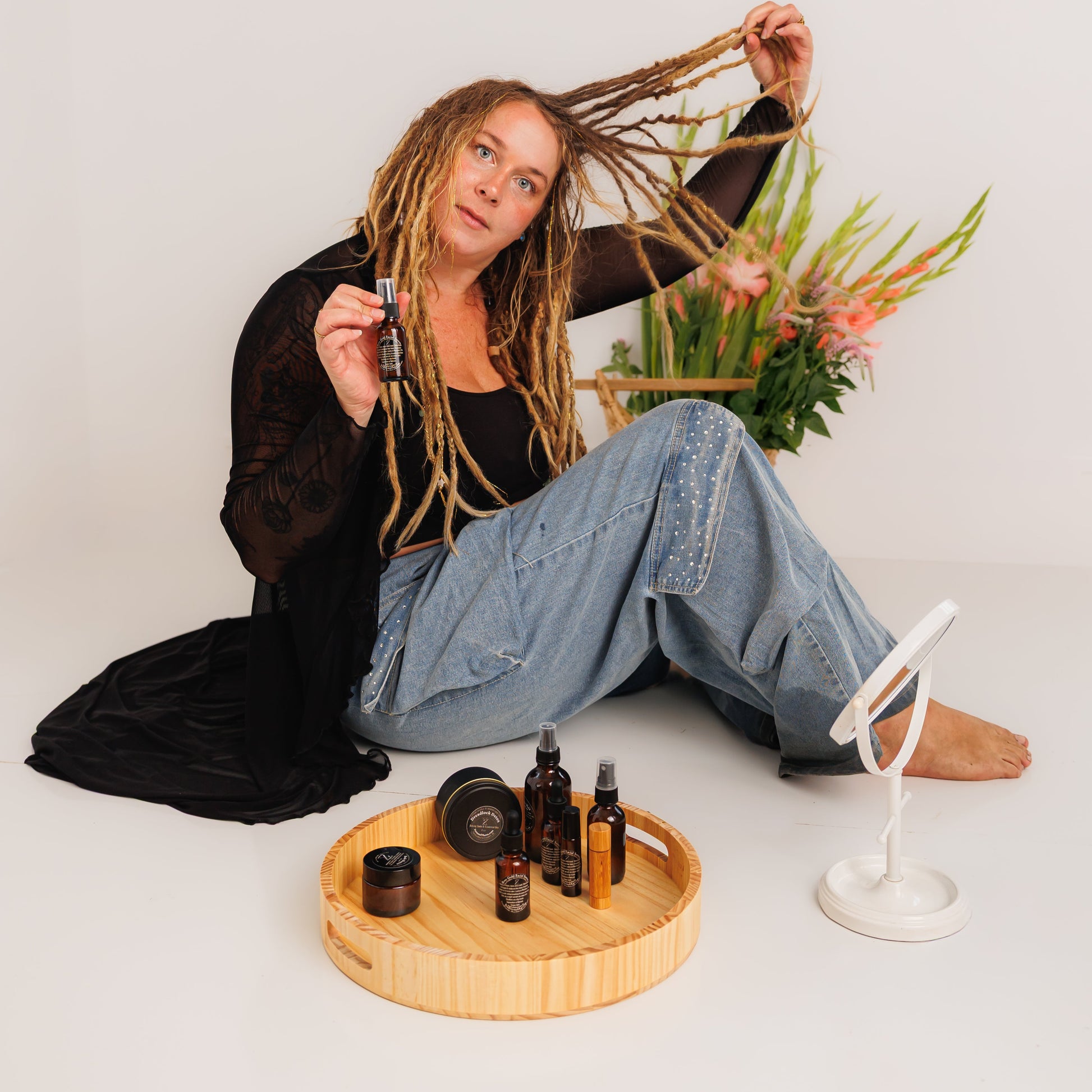 Person with dreaded hair sitting on the floor with hair care products and a plant.