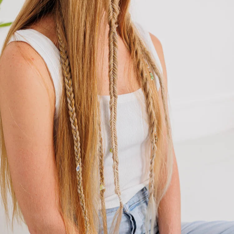 Person with braided hair wearing a white top and light blue jeans on a plain background