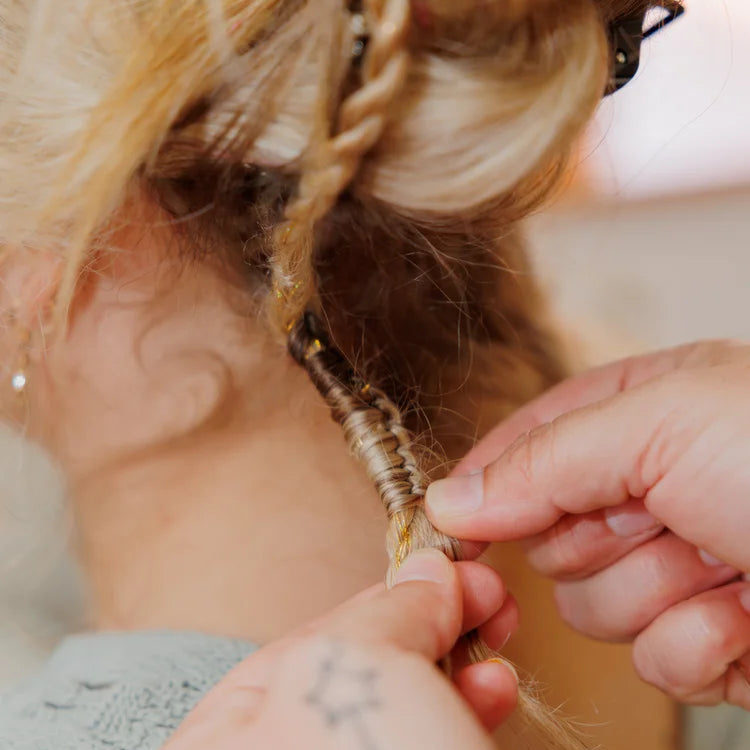 Close-up of hands braiding a person's hair with a blurred background