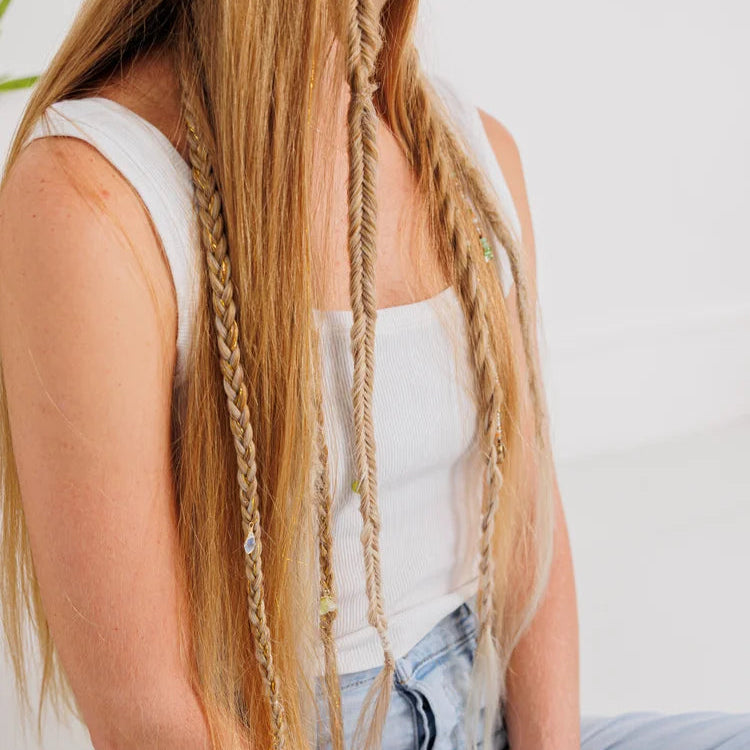 Person with braided hair wearing a white top and light blue jeans on a plain background
