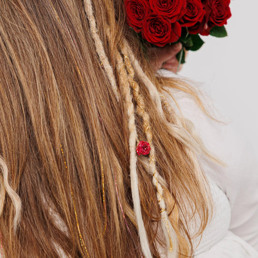 Person with dreads and braided hair extesnions holding a bouquet of red roses against a white background