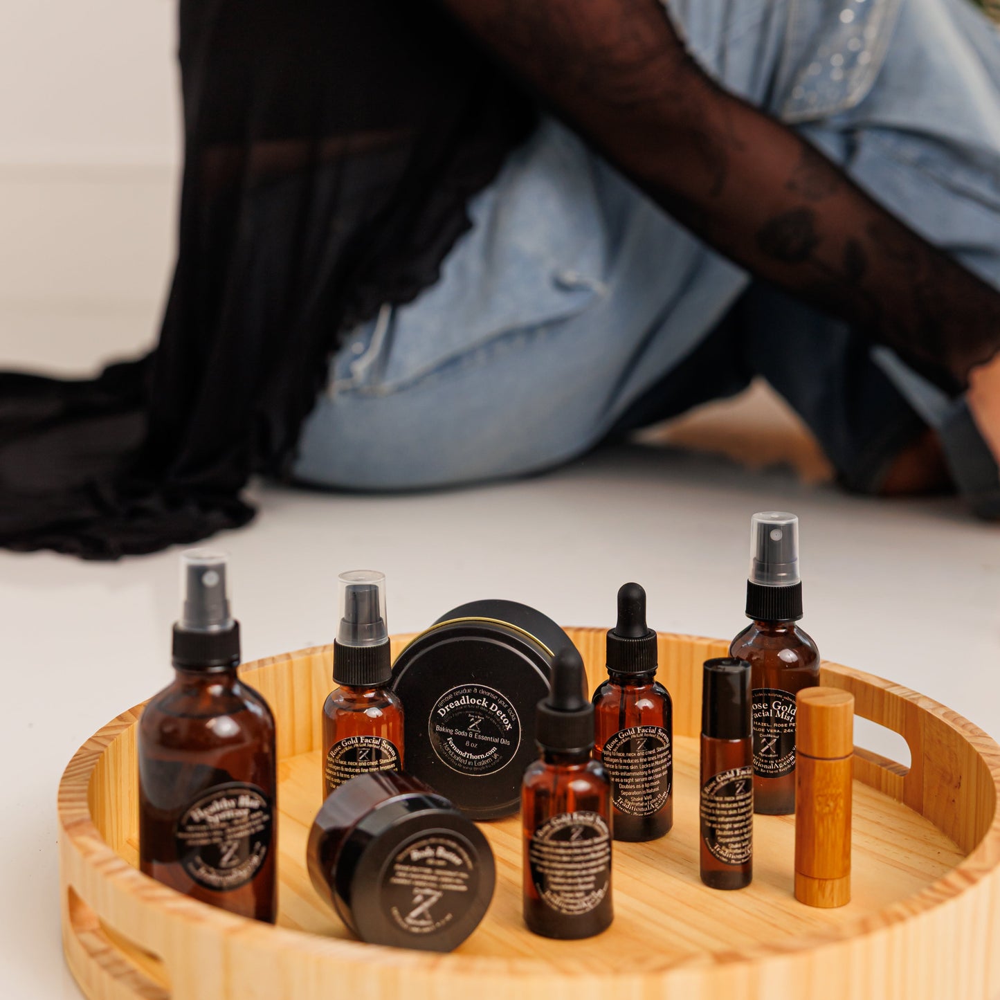 Collection of dreadlock care products on a wooden tray with a person sitting in the background.
