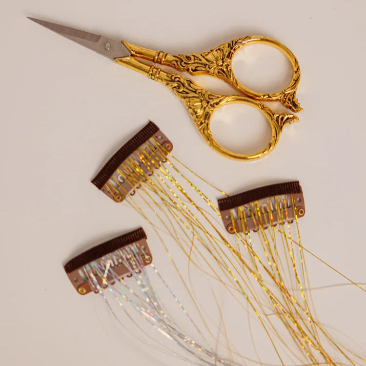 Gold scissors with decorative fairy hair clip ins extensions on a light background