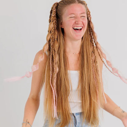 Person with long braided hair laughing against a plain background