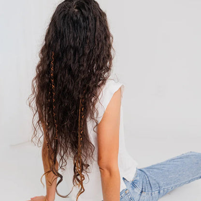 Person with long, wavy boho hair extension sitting on a white floor against a white wall.