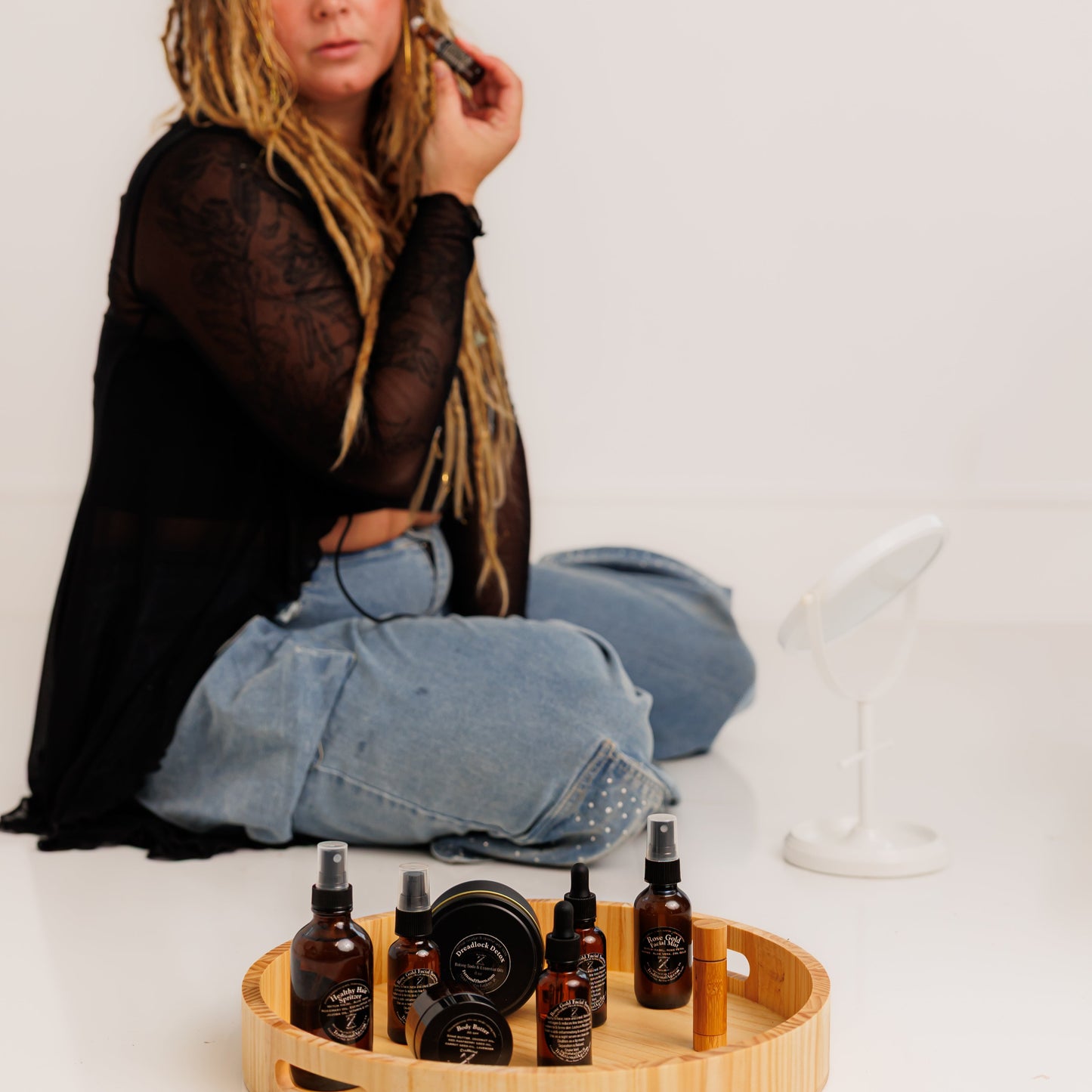 Woman sitting on the floor with a tray of deadlocks detox products on a white background