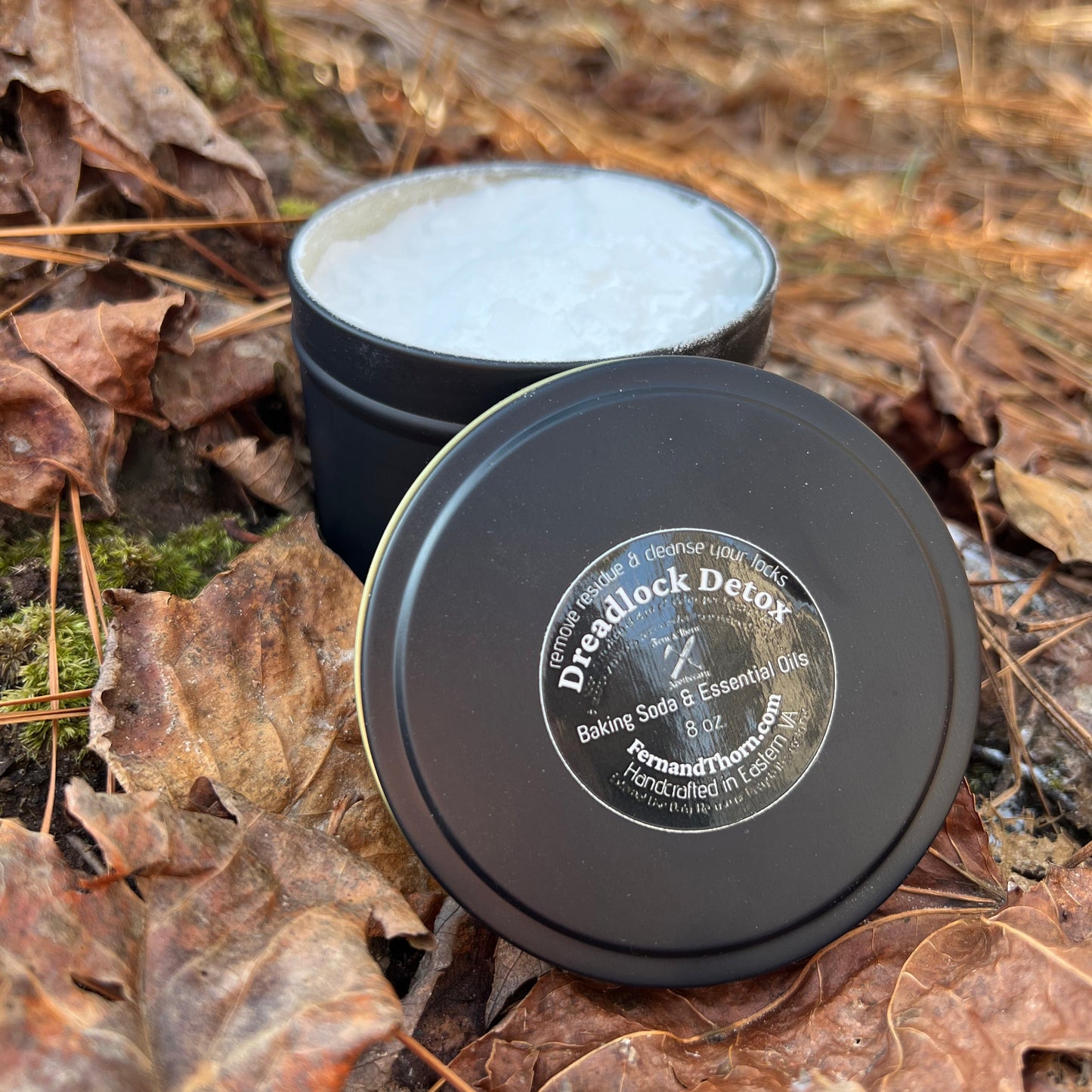 opened container of a dreadlock detox with a label on a forest floor with leaves and tree trunks.
