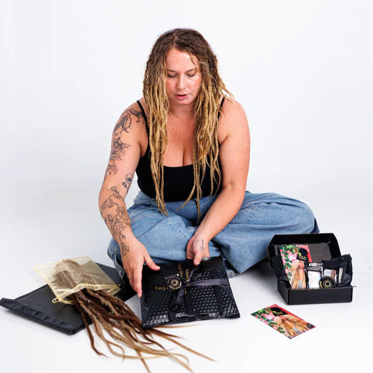 Person with dreadlocks sitting on the floor with a hair care kit on a white background