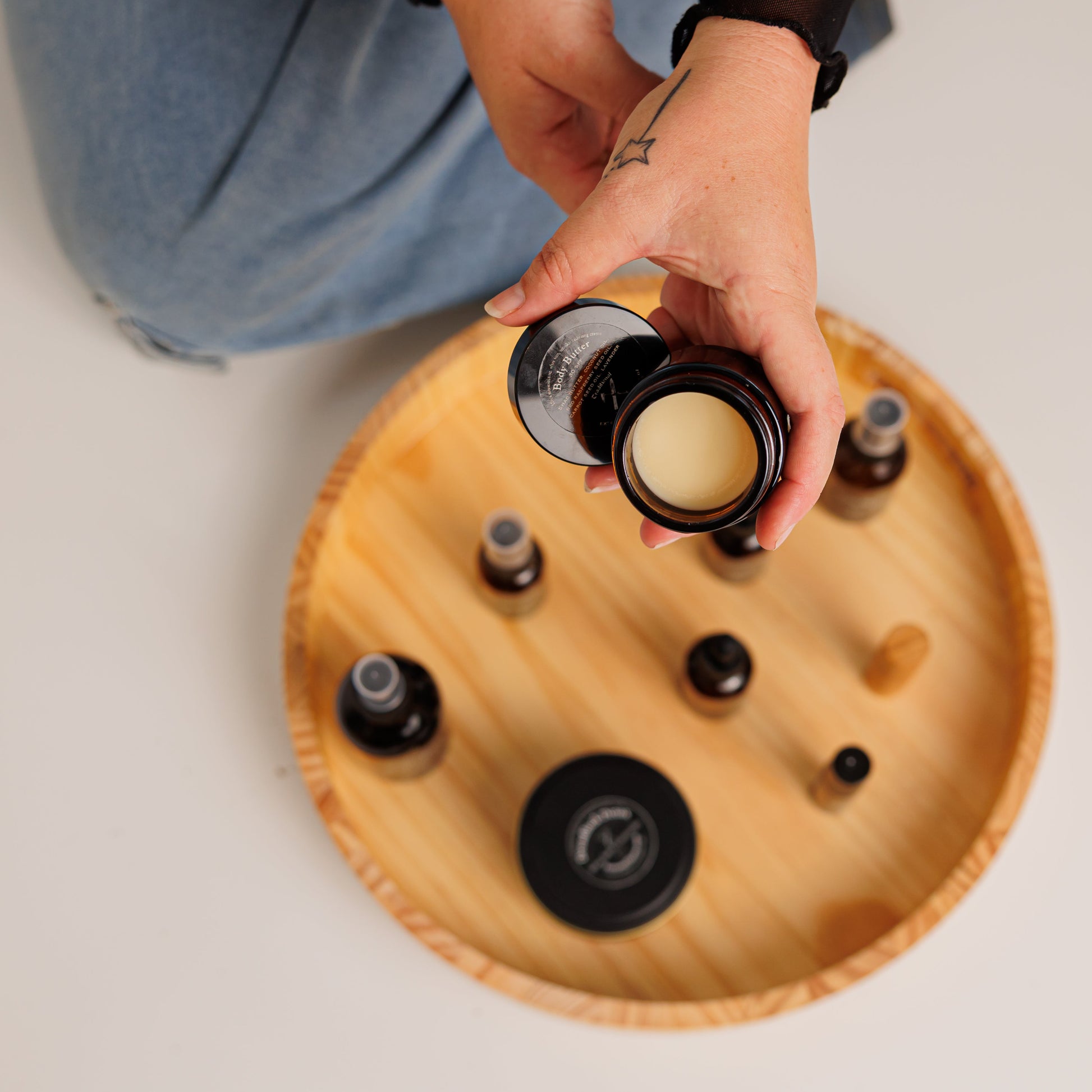 Person holding a container of dreadlock detox over a wooden tray with various items on a light background