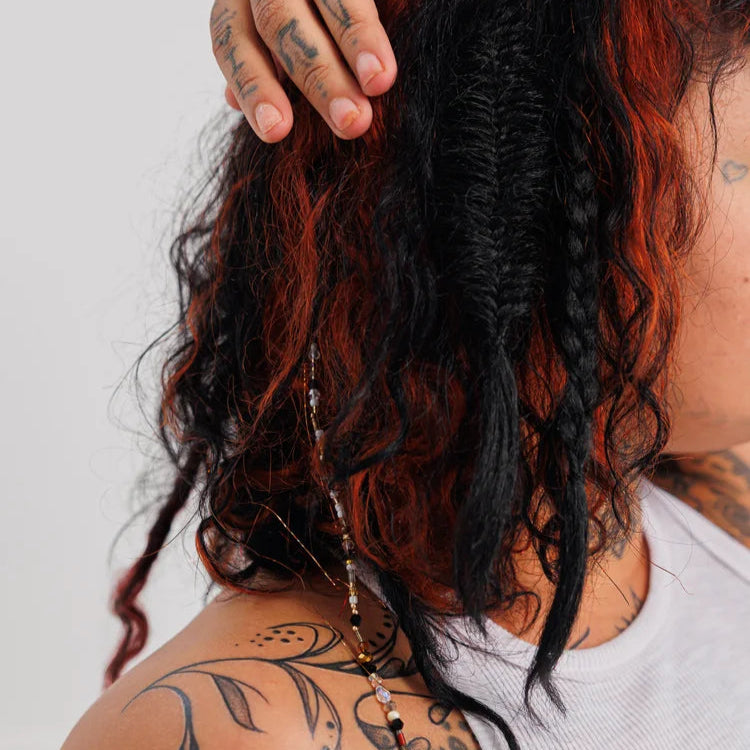 Person with red and black hair, tattoos on neck and shoulder, wearing a fairy chains