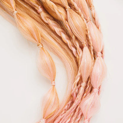 Close-up of braided hair extensions with a gradient of pink and blonde colors on a light background.