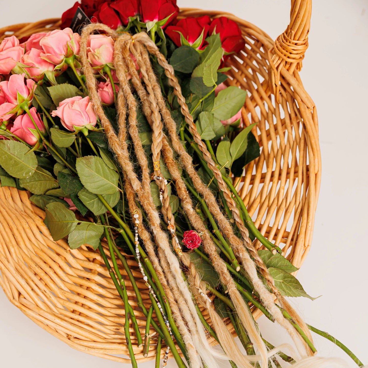 blonde dreadlock extensions and braids displayed in a rustic basket surrounded by rose stems and leaves
