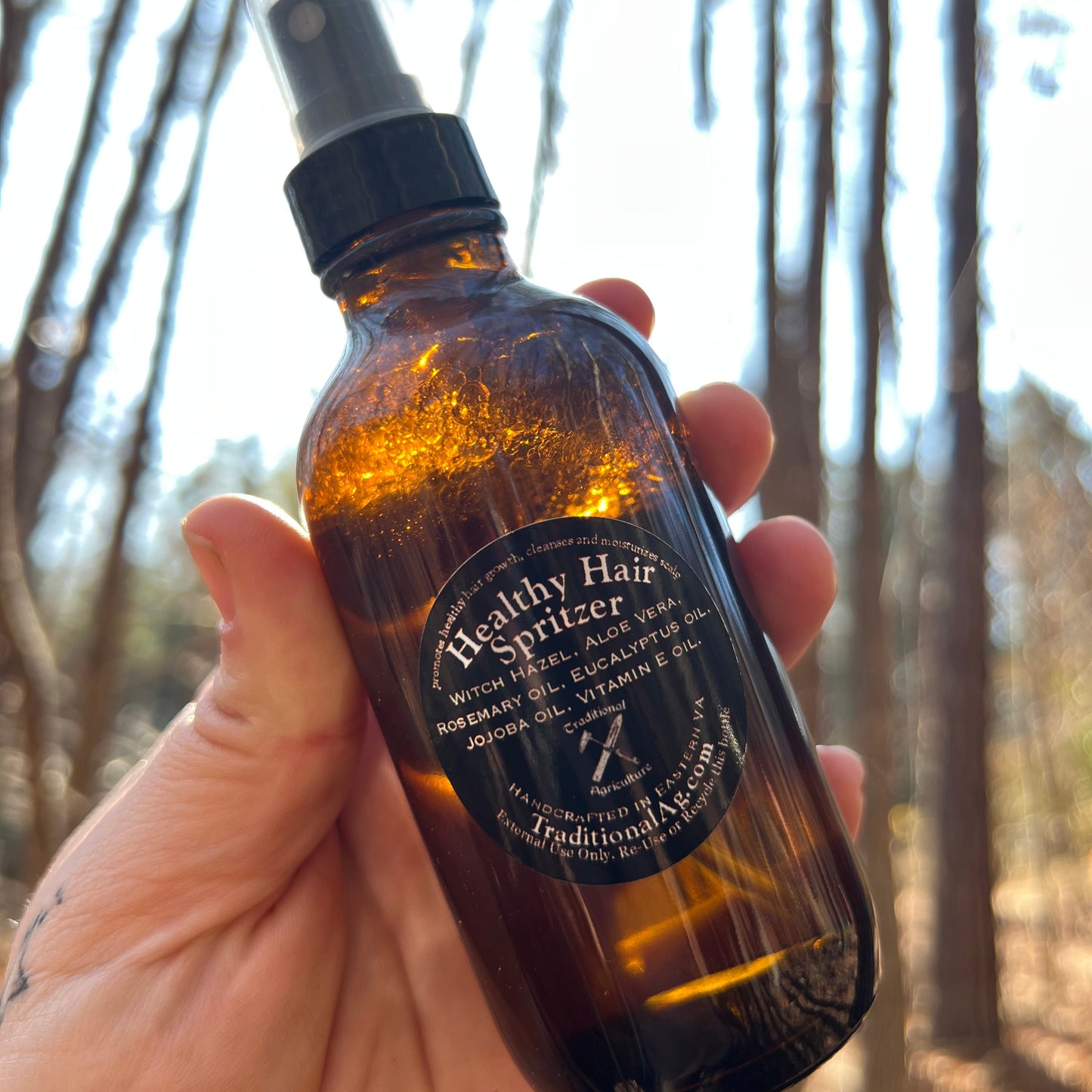 Hand holding a healthy hair spritz bottle with a label against a blurred natural background