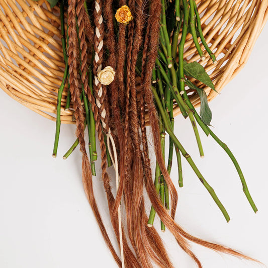 light natural red braided hair extensions with green leaves on a woven basket against a white background