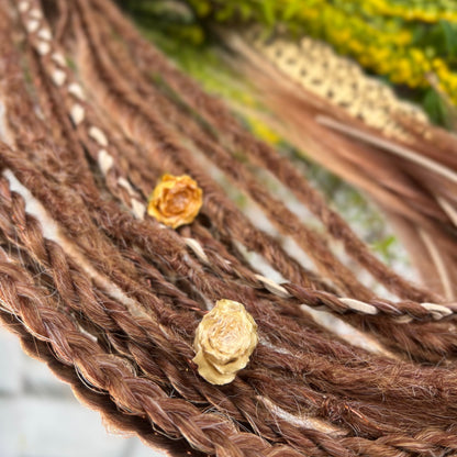 Close-up of braided dreadlocks with small yellow flowers on a blurred natural background