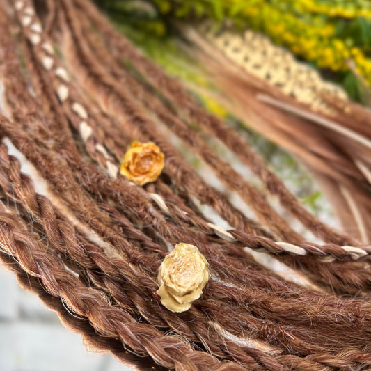 Close-up of braided dreadlocks with small yellow flowers on a blurred natural background