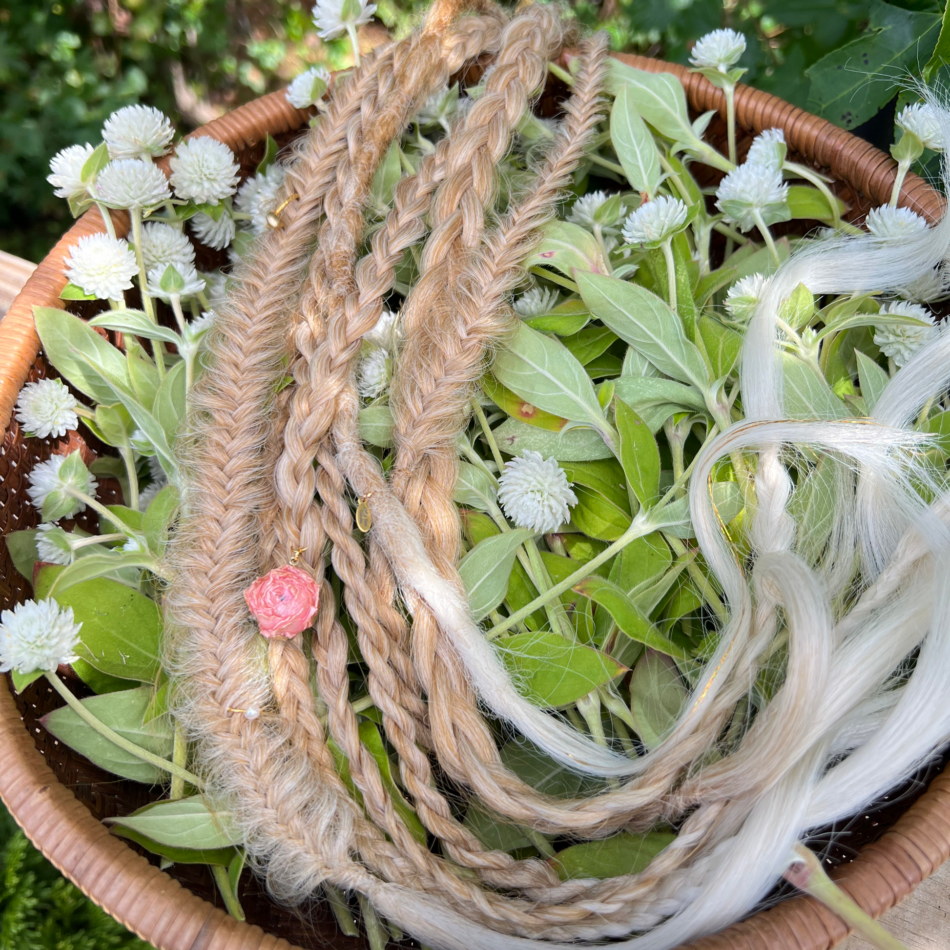 Braided hair extension with a pink bead on a bed of greenery