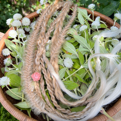 Braided hair extension with a pink bead on a bed of greenery