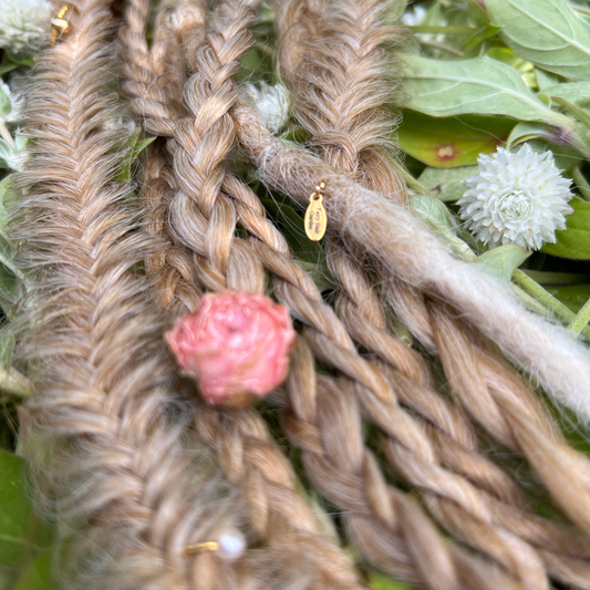 dreads and braided hair with a pink flower and gold hair tie against a green leafy background