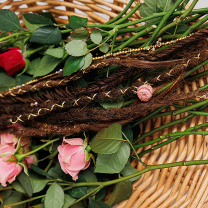 brown dreadlock and braid set in a woven basket surrounded by rosebuds, leaves, and twine