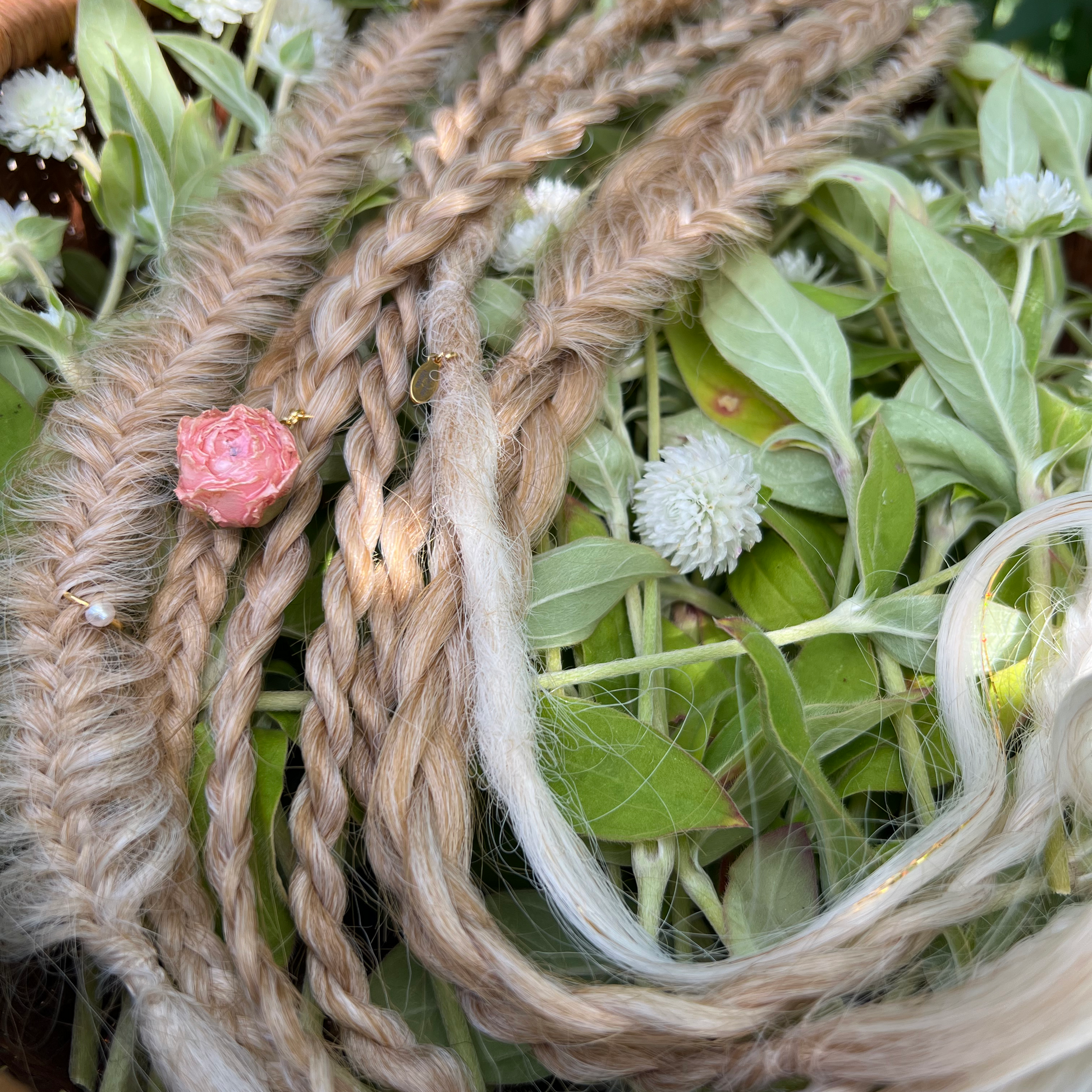 blond braided hair with pink flower and green leaves in a woven basket