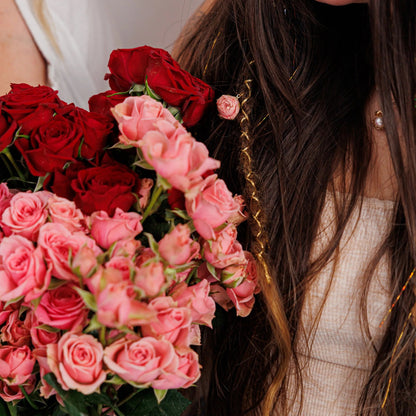 Close-up of bouquet with pink and red roses held by woman with boho hair and golden strand